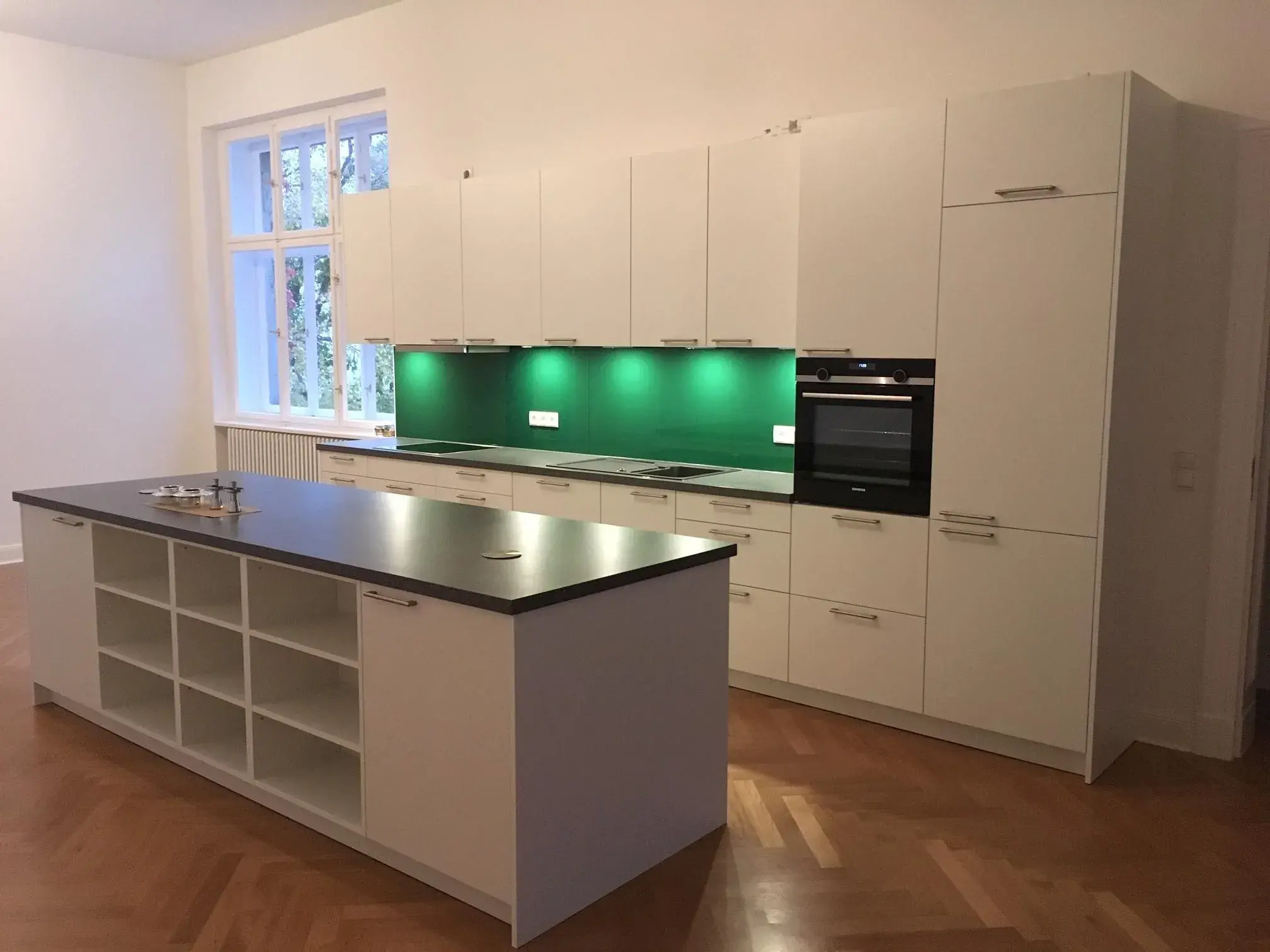 Küchenzeile weiß mit Nischenrückwand grün glänzend plus Kücheninsel mit offenen Regalfächern und Arbeitsplatte dunkel